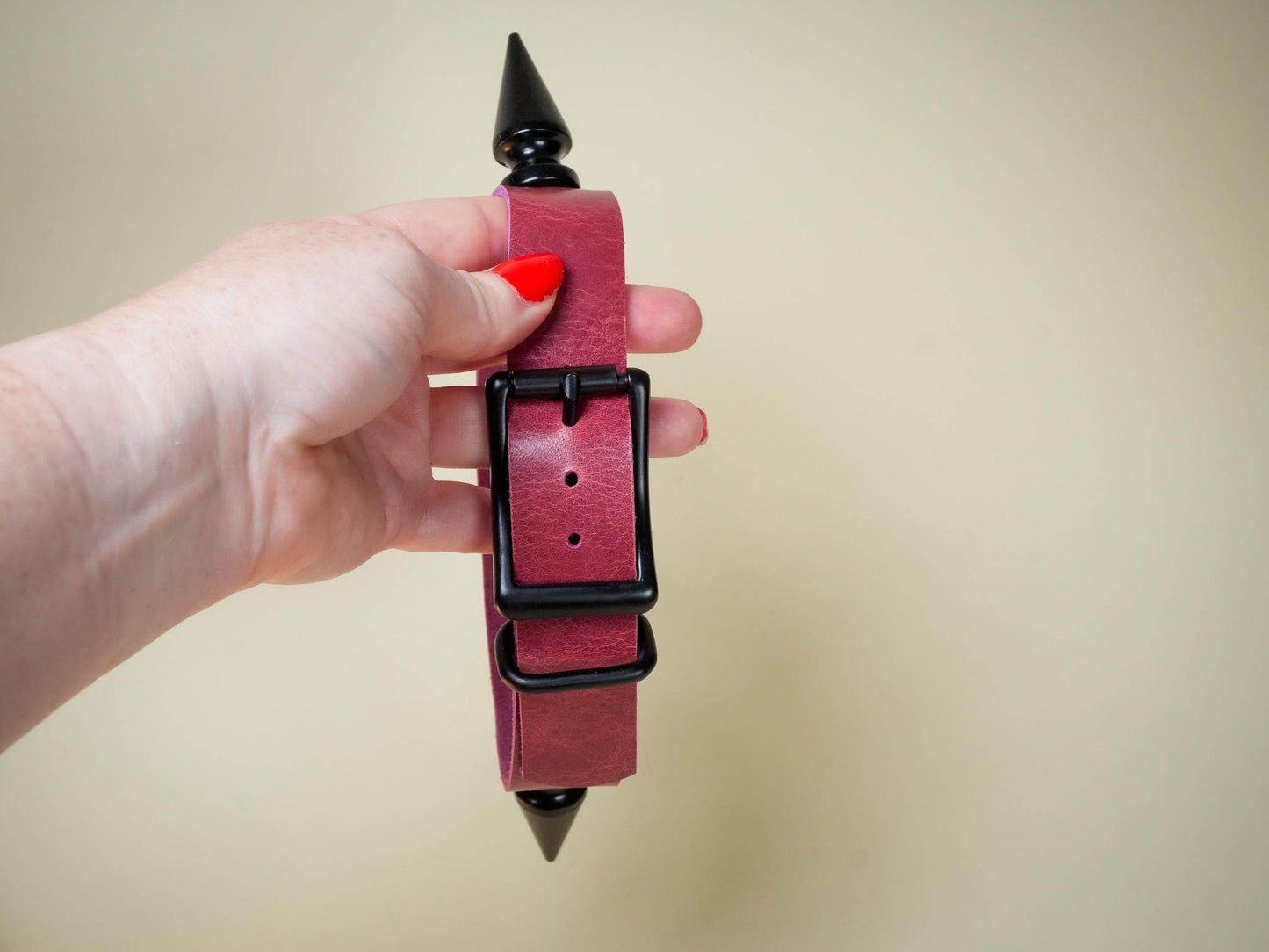 Hand holding a burgundy rave choker with black buckle and pointed studs by Bound by Dave