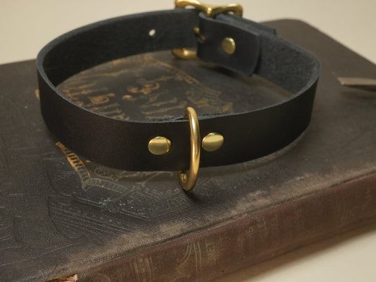 Black leather flogger collar with gold hardware displayed on an antique book background
