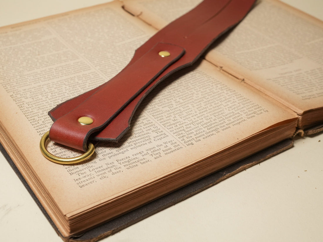 Leather BDSM paddle with brass hardware placed on an open vintage book background