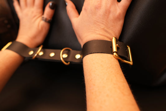 Close-up of durable high-quality leather cuffs with gold hardware on wrists against a black background