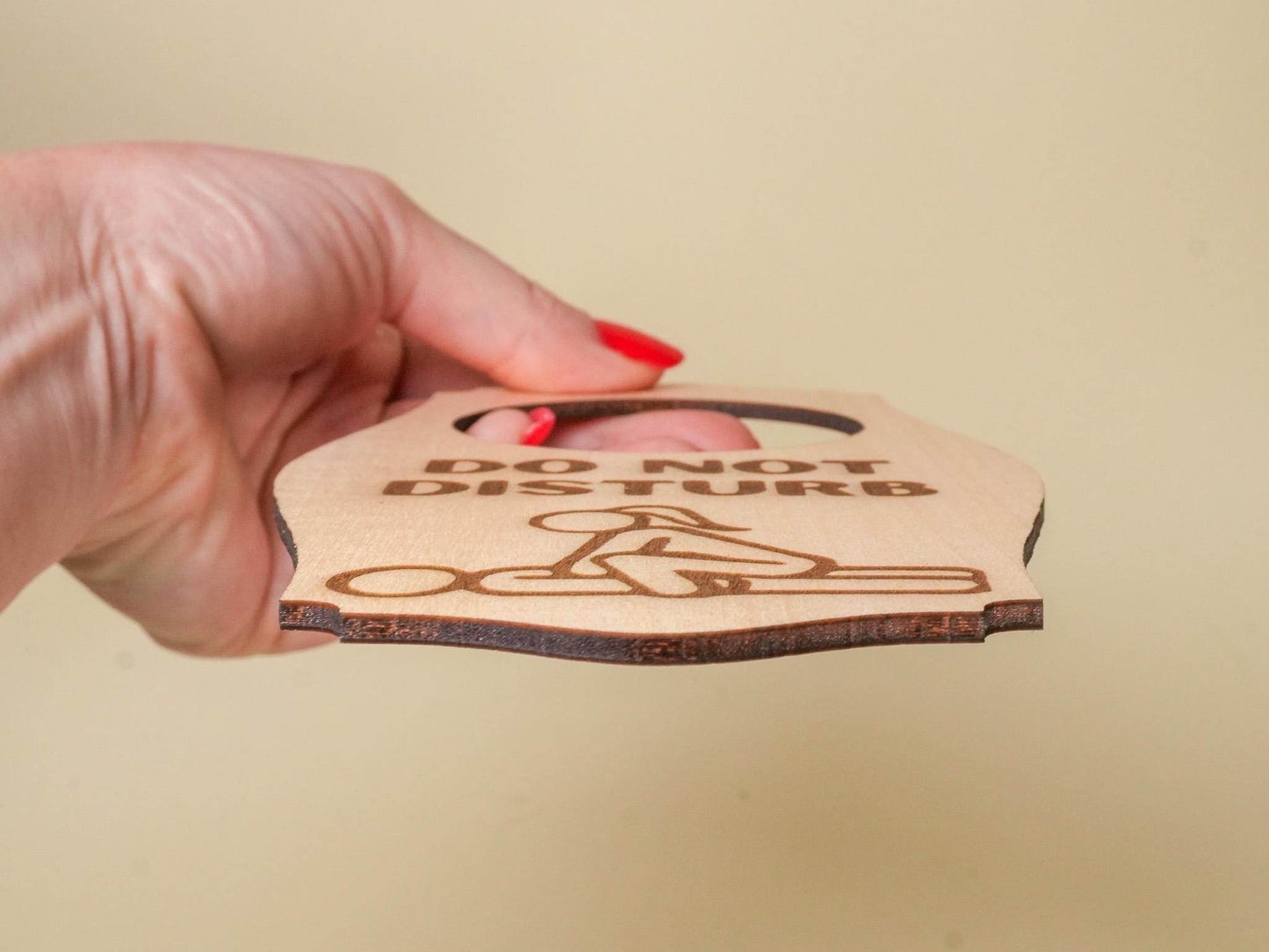 Hand holding a wooden adult do not disturb sign with engraved text and finger graphic