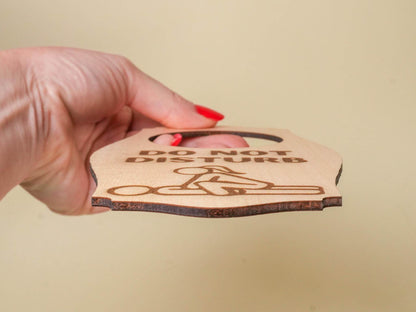 Hand holding a wooden adult do not disturb sign with engraved text and finger graphic