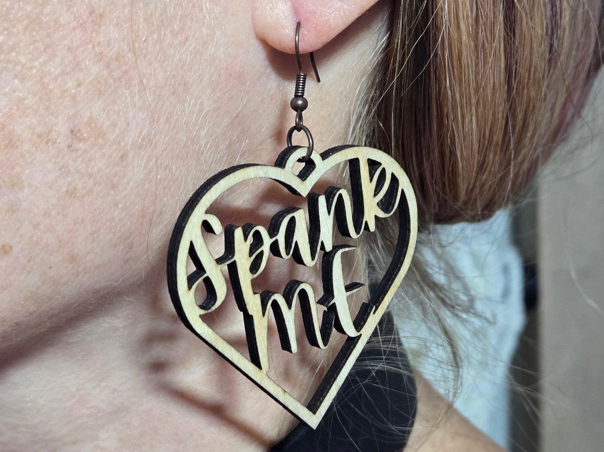 Wooden heart-shaped bdsm earrings with spank me cutout worn on ear by Bound by Dave