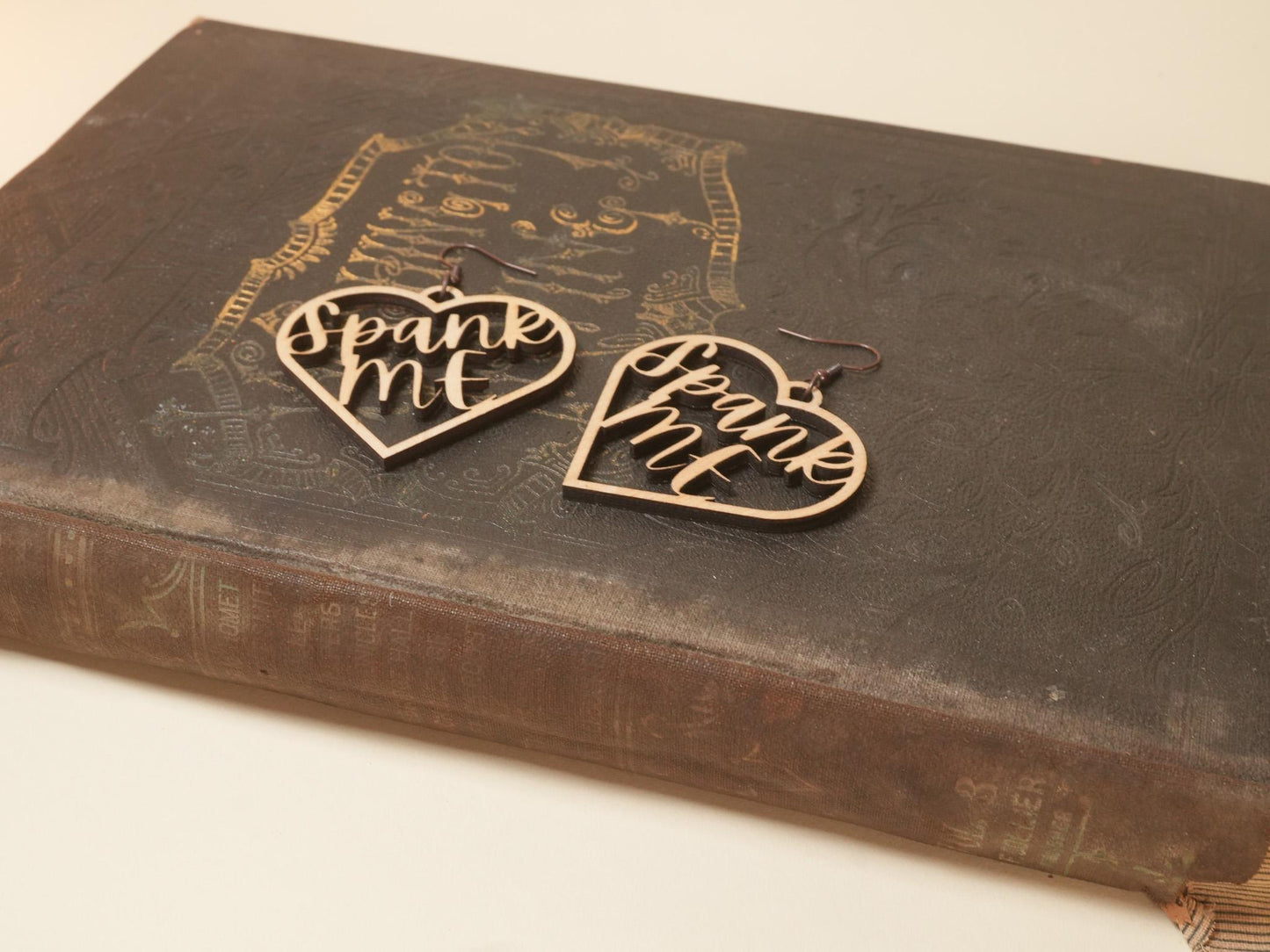 Bound by Dave wooden heart-shaped bdsm earrings with prank me text on an old book