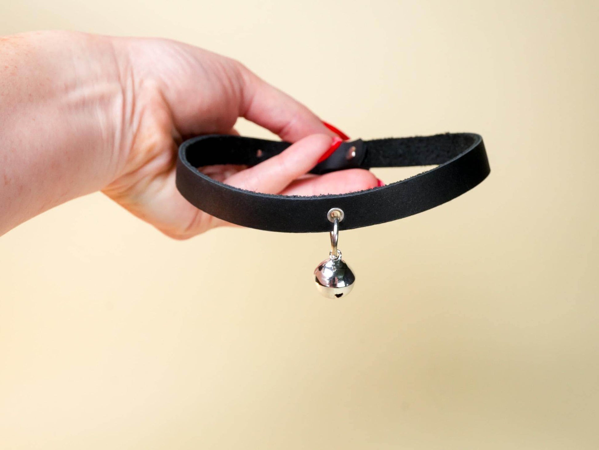 Black kitten collar with small silver bell held by hand against beige background