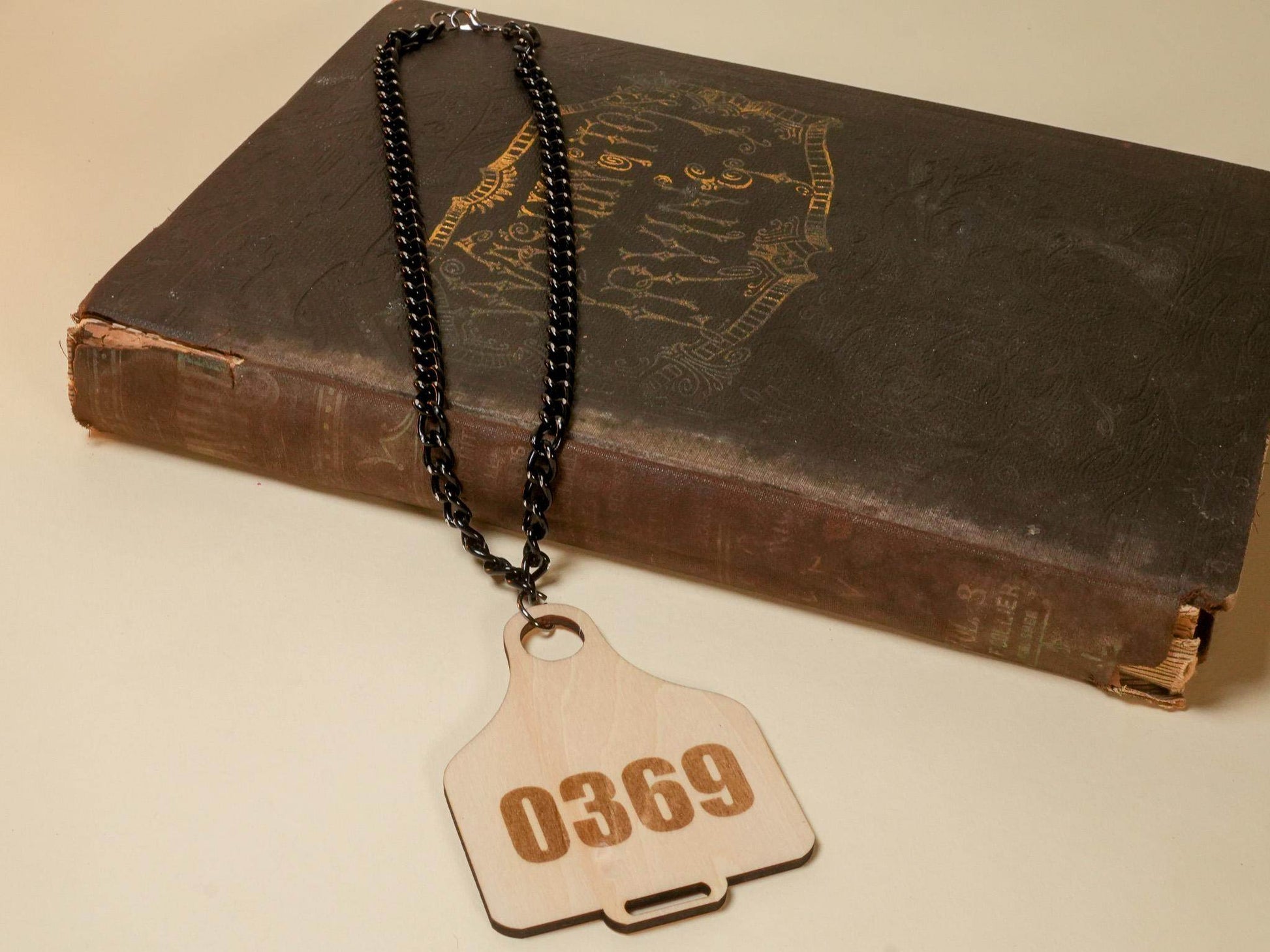 Bound by Dave wooden Cow Tag necklace with number 0369 on black chain placed on vintage book