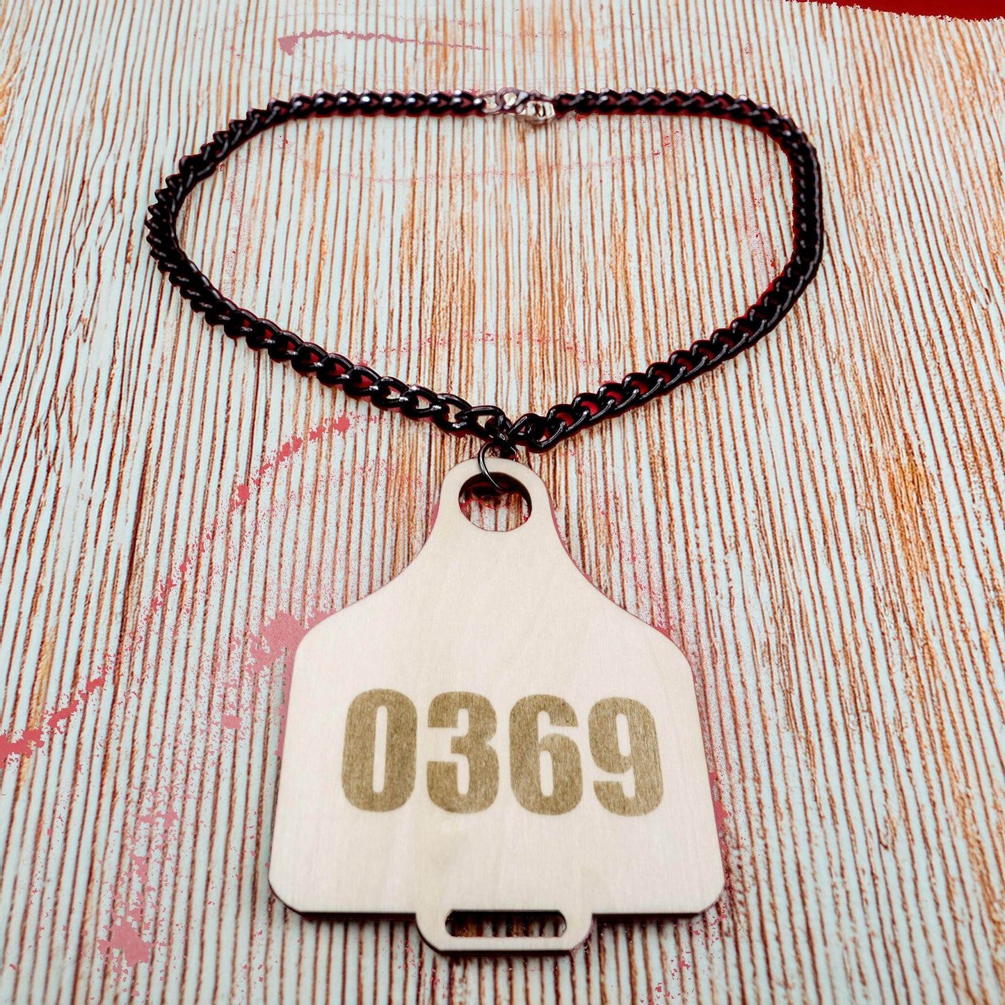 Cow Tag necklace with number 0369 on light wood tag attached to black chain by Bound by Dave
