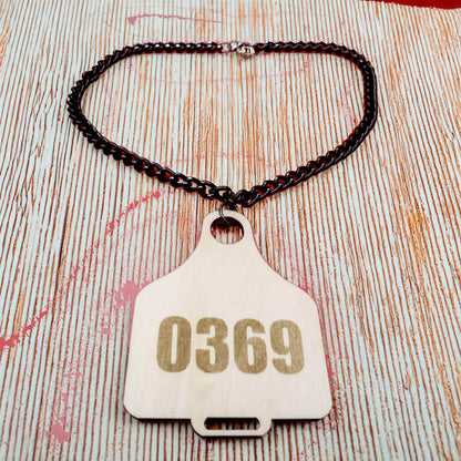 Cow Tag necklace with number 0369 on light wood tag attached to black chain by Bound by Dave