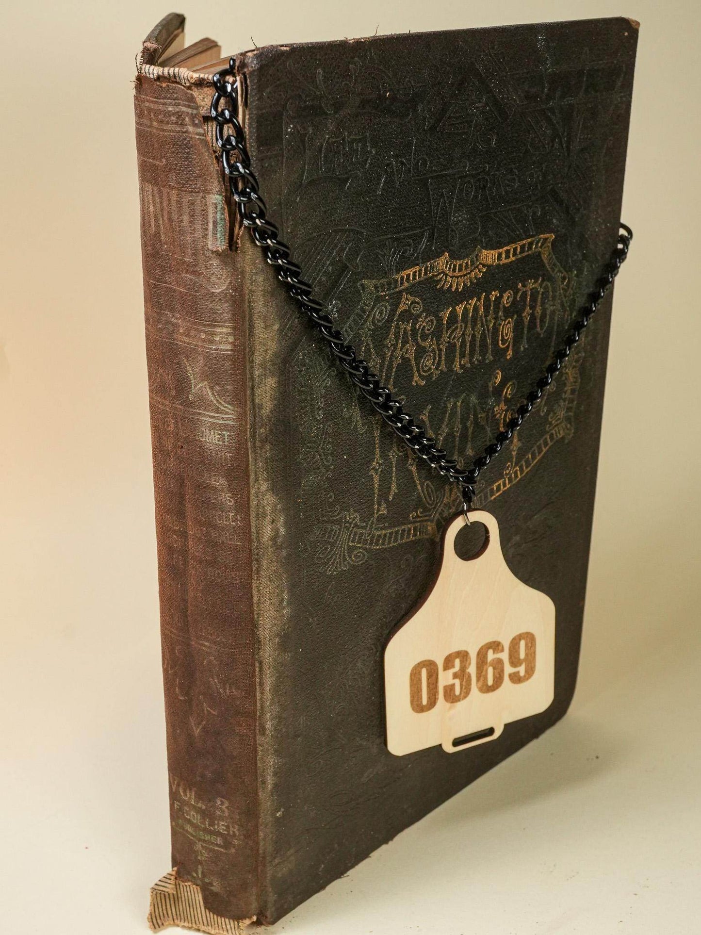Cow Tag number 0369 with black chain hanging on a vintage book by Bound by Dave
