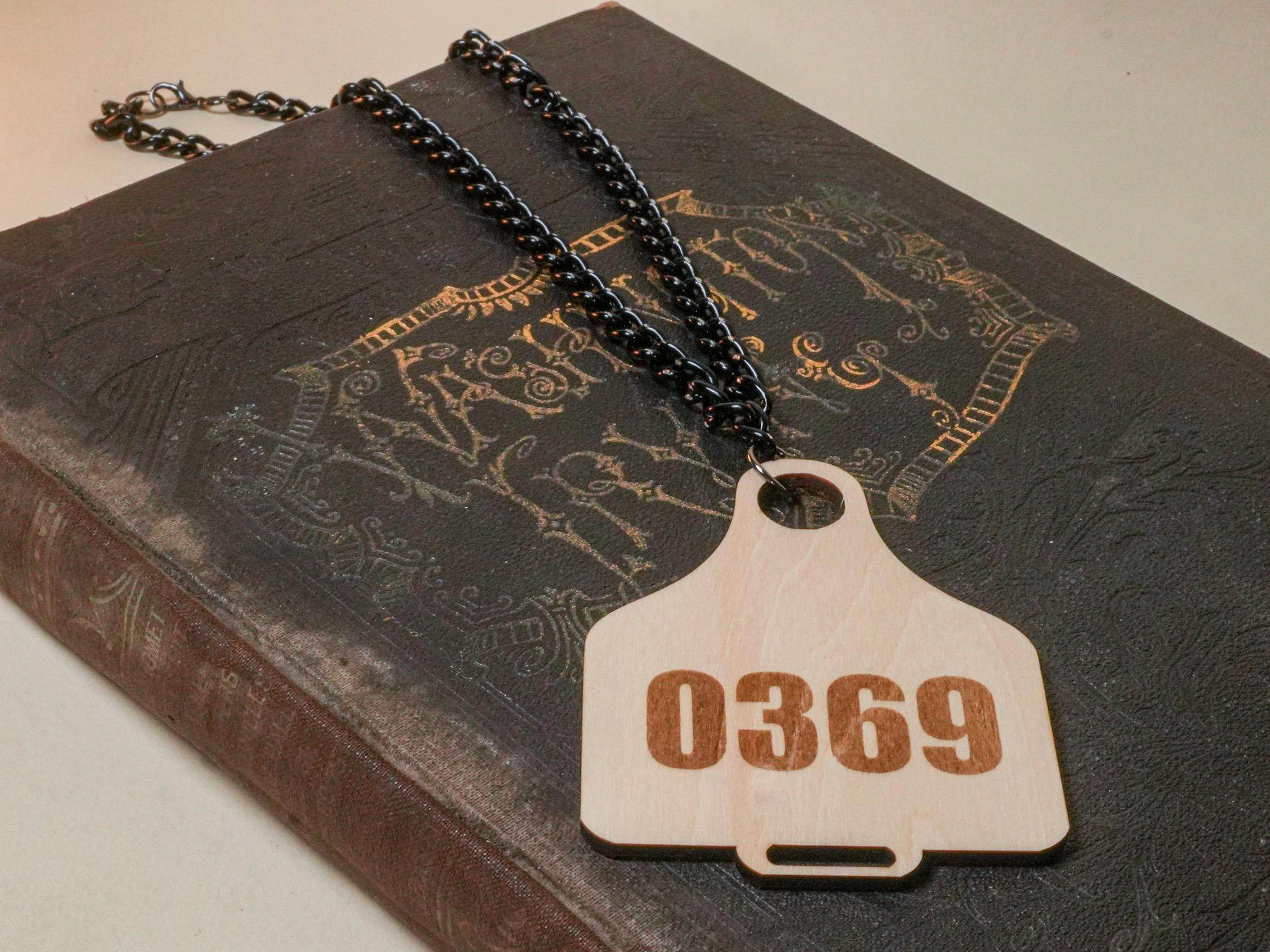 Bound by Dave wooden Cow Tag necklace with number 0369 on black chain on vintage book