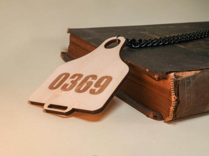 Bound by Dave wooden Cow Tag with number 0369 and black chain on a vintage book
