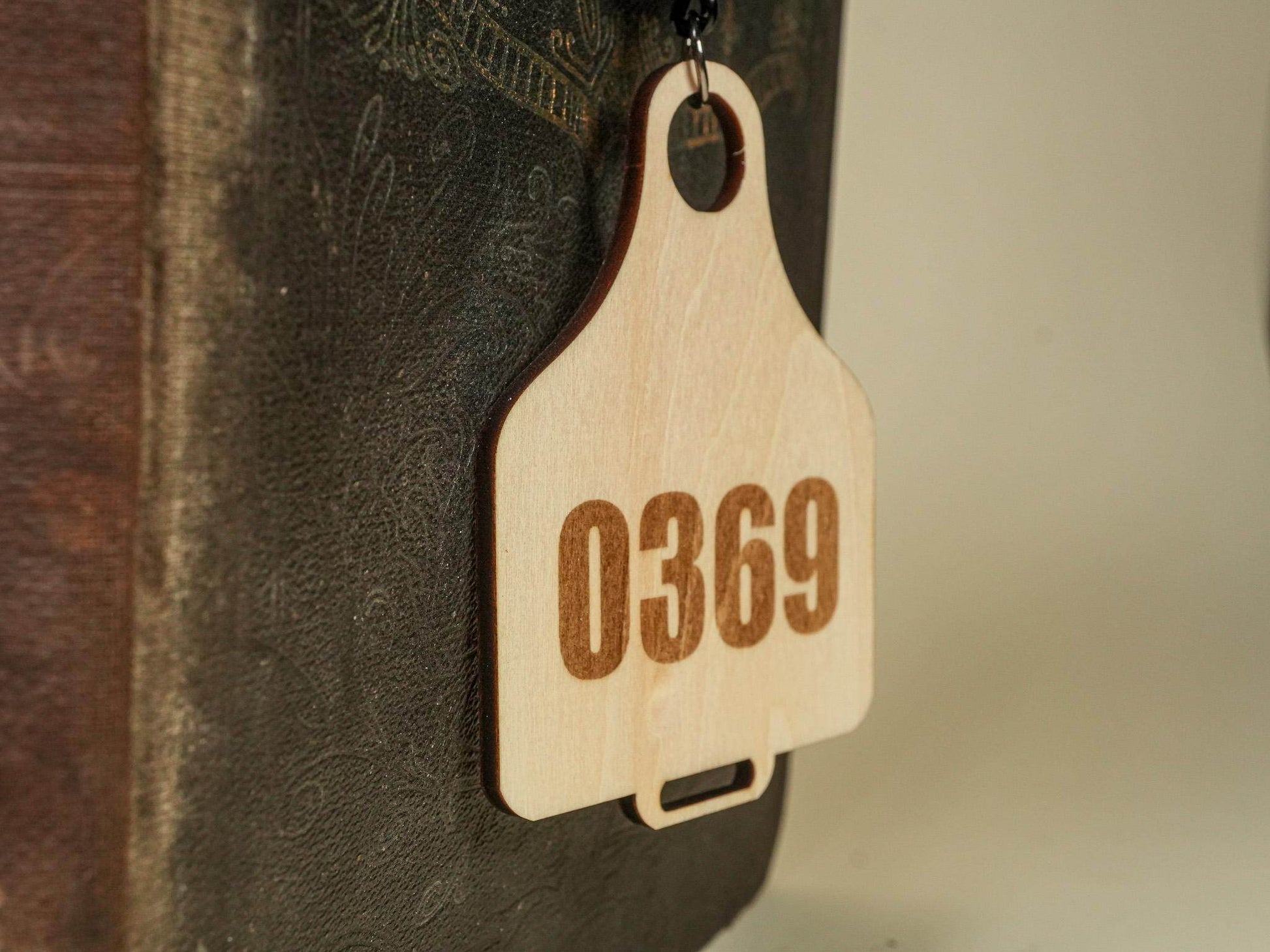 Wooden Cow Tag with number 0369 engraved hanging against a dark textured background