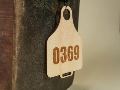 Wooden Cow Tag with number 0369 engraved hanging against a dark textured background
