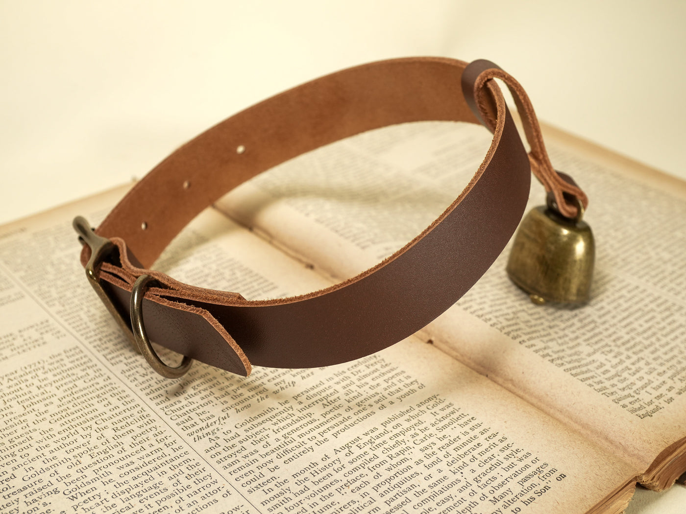 Bound by Dave leather dog collar with attached small brass cowbell on vintage book background