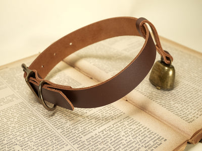 Bound by Dave leather dog collar with attached small brass cowbell on vintage book background