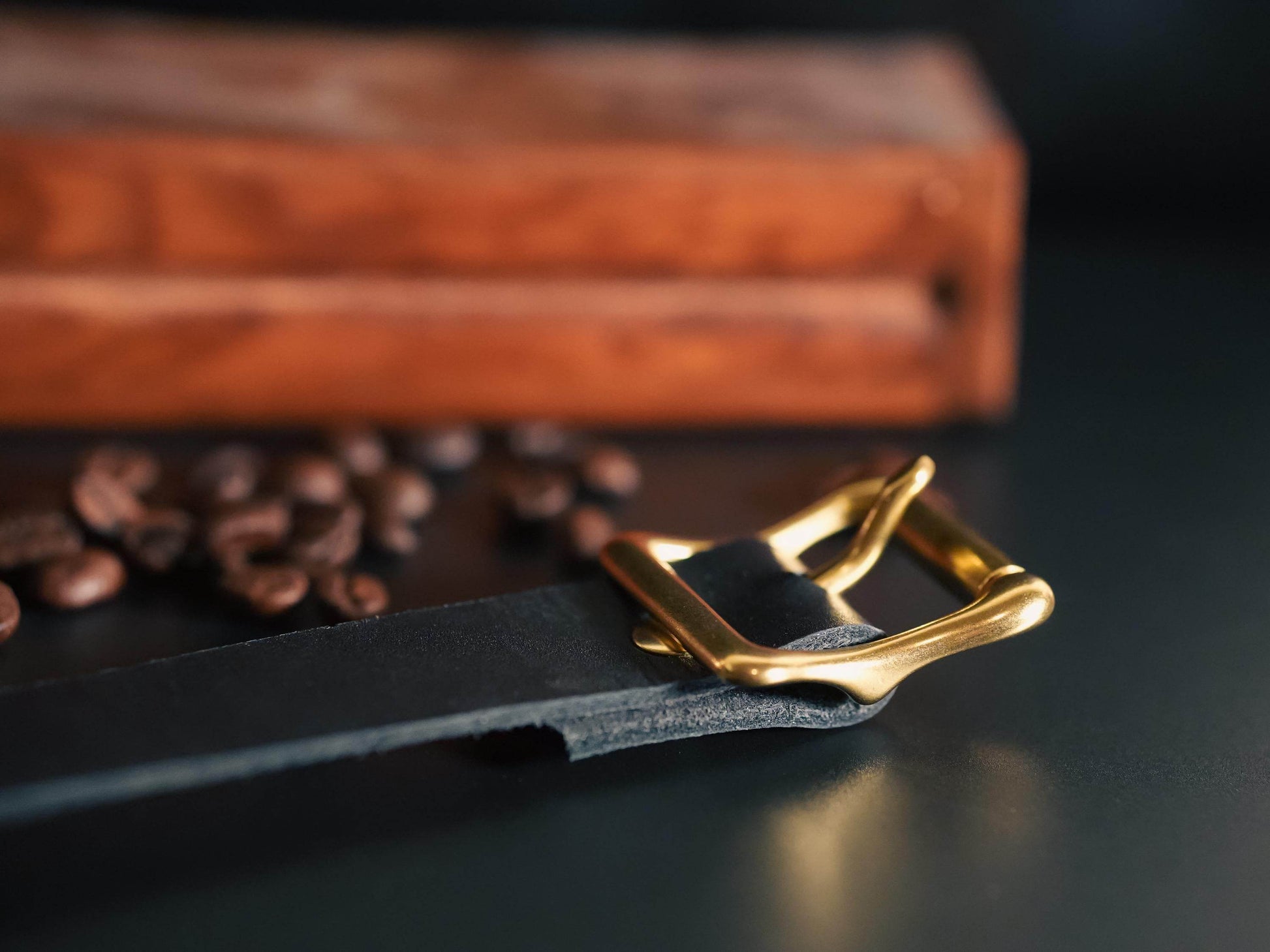 Bound by Dave black leather day collar with gold buckle on dark surface with coffee beans
