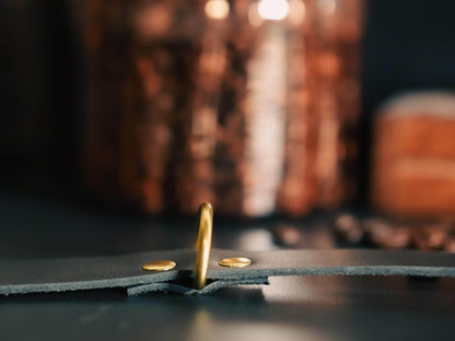 Close-up of Bound by Dave leather day collar with gold metal ring and rivets on dark background