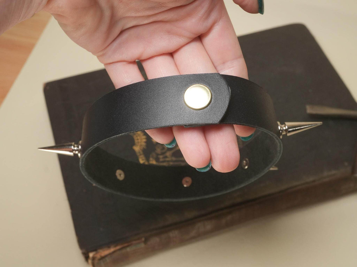 Black leather Goth Choker with metal spikes and button clasp held in hand over vintage book