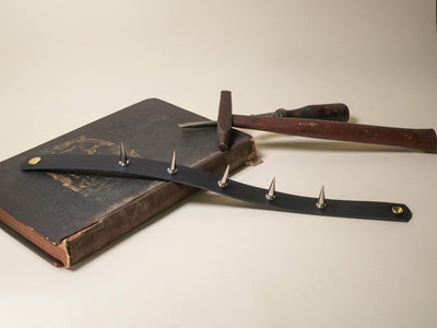 Bound by Dave black leather Goth Choker with silver spikes resting on old book with hammer