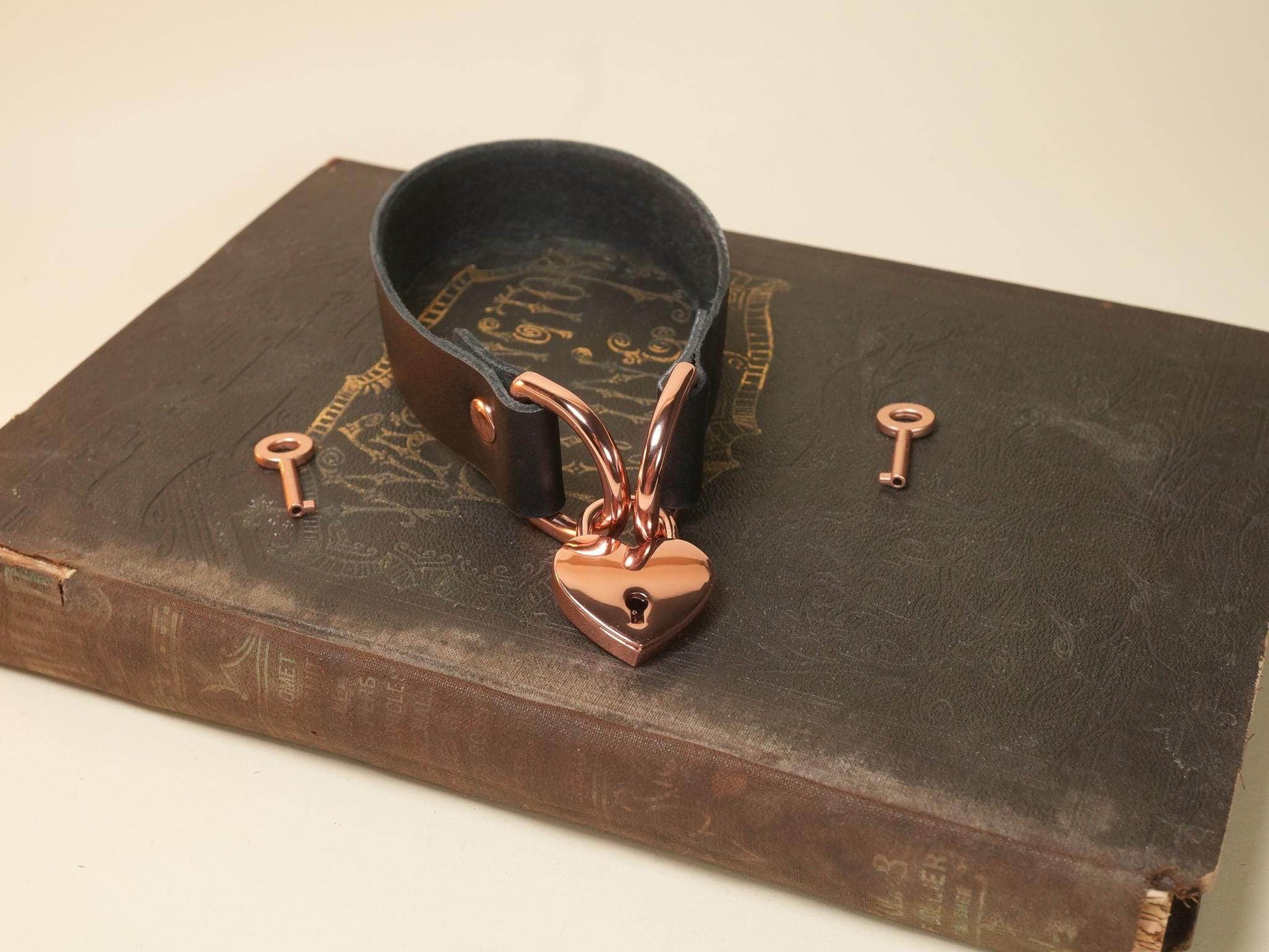 Black leather cuff bracelet with rose gold Heart Lock and two matching keys on vintage book