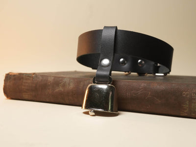 Black leather hucow collar with silver bell attached displayed on old brown book