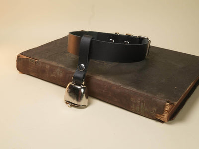 Leather hucow collar with metal cowbell by Bound by Dave placed on an old worn book