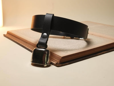 Bound by Dave black leather hucow neck strap with metal cowbell on an open book