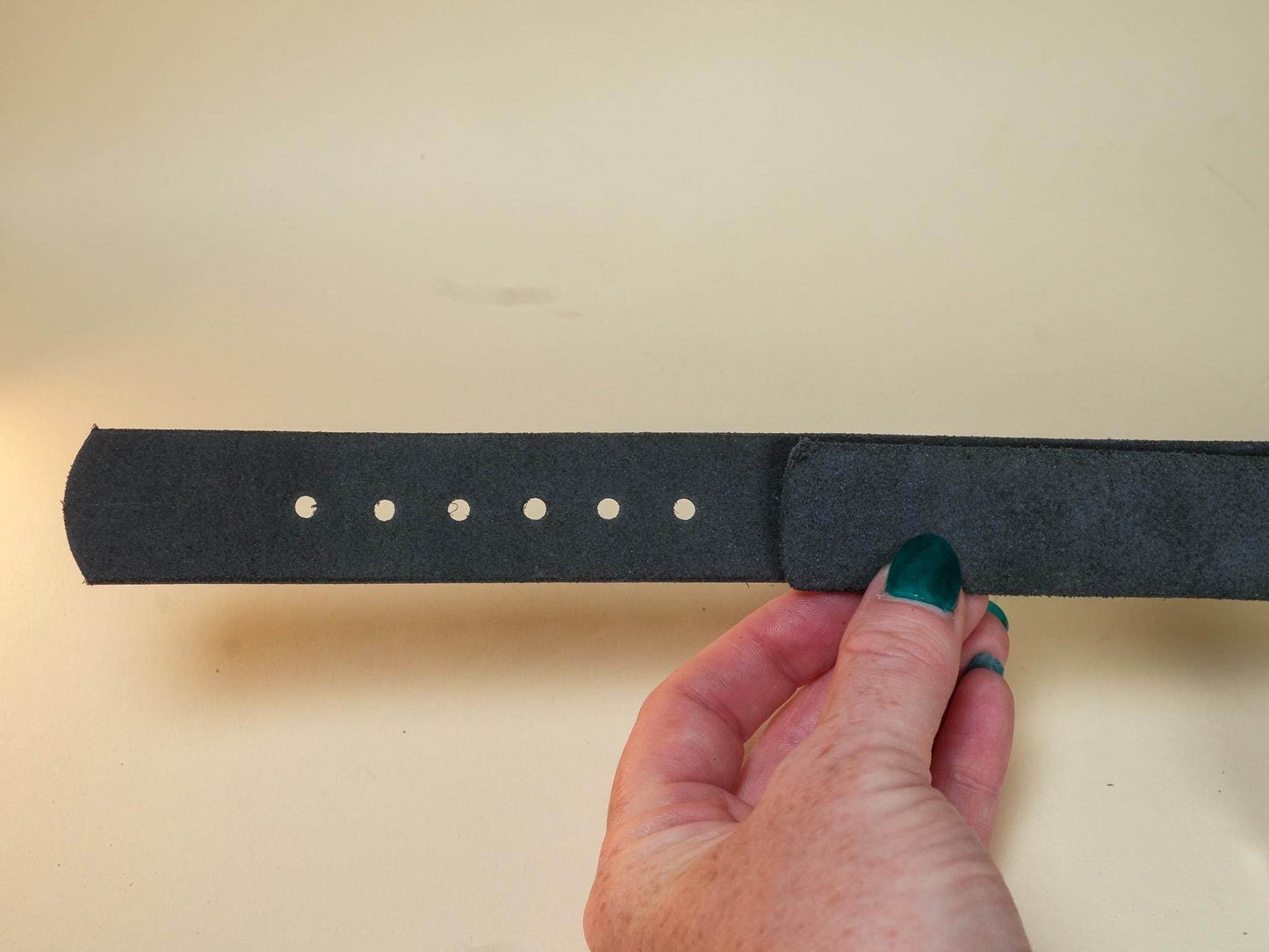 Hand holding a black hucow belt with multiple adjustment holes against a neutral background