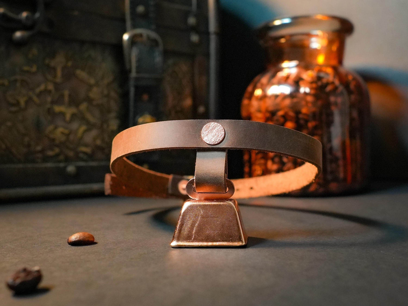 Brown leather hucow choker with metal bell by Bound by Dave on dark surface