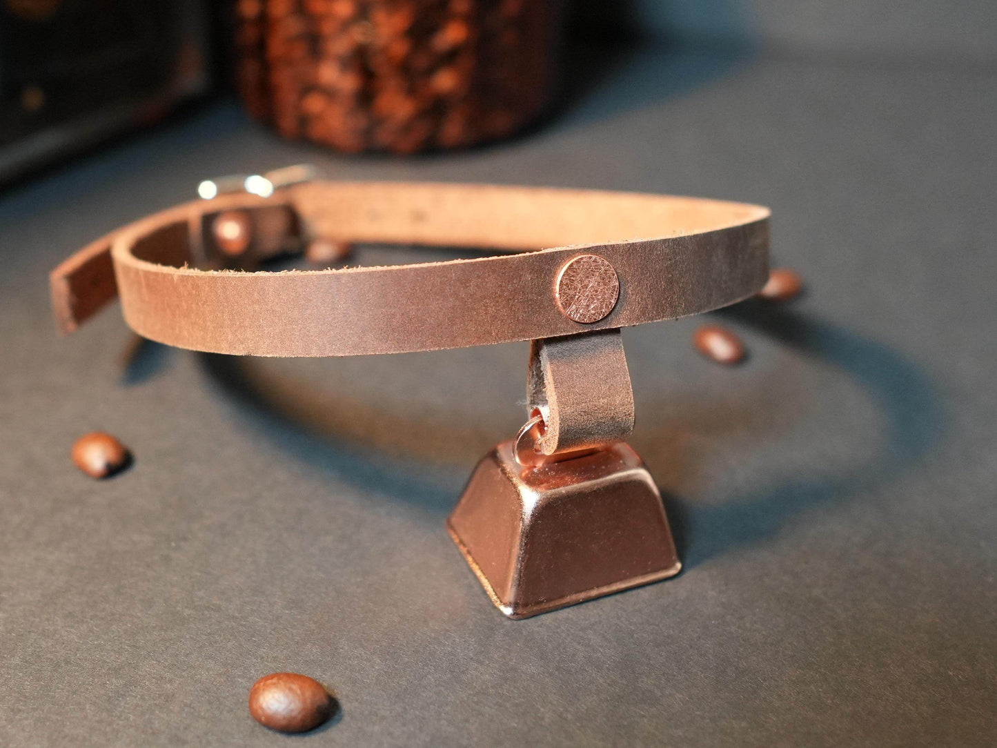 Bound by Dave brown leather hucow choker with metal cowbell on gray surface