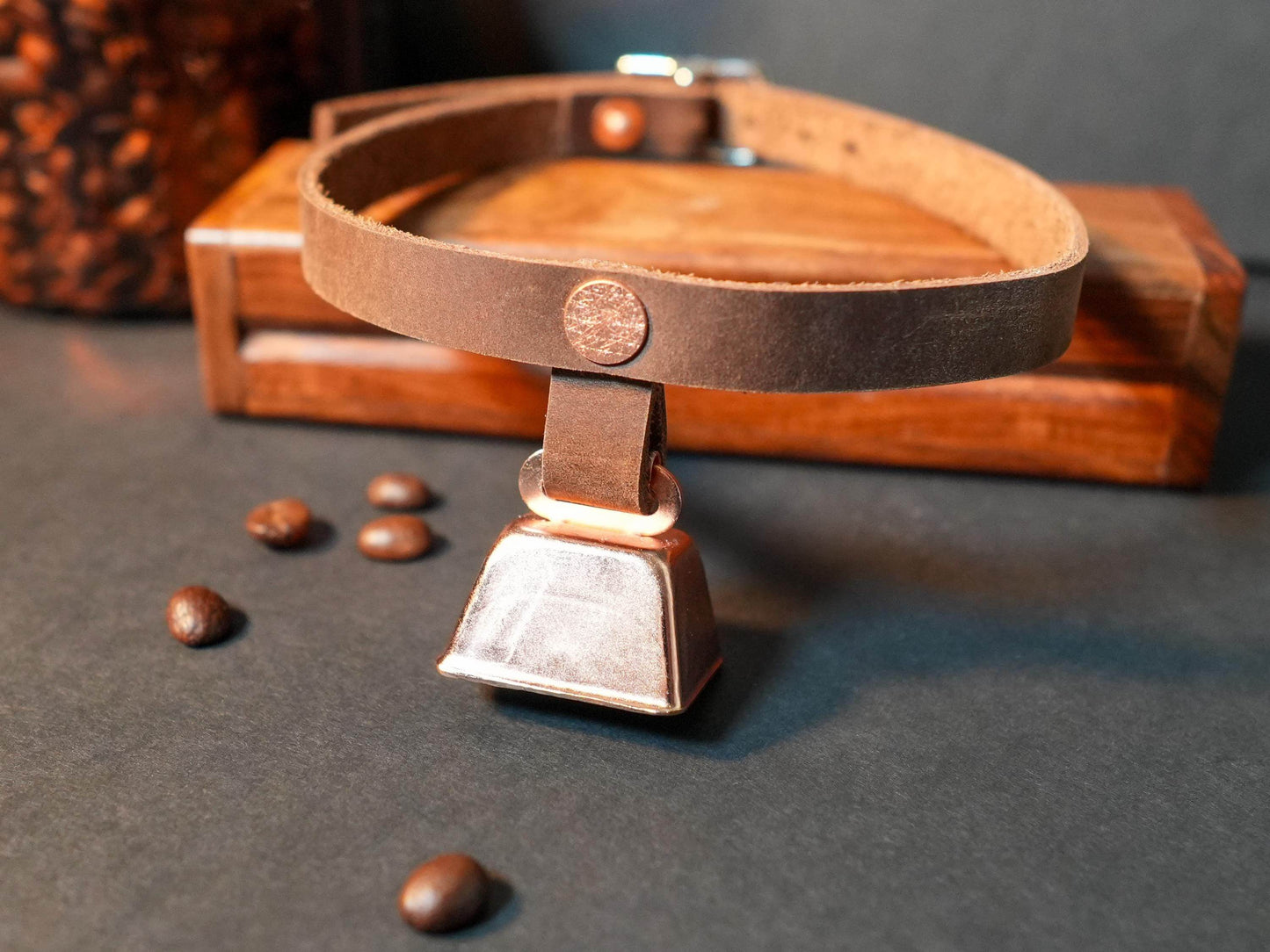 Brown leather hucow choker with a metal cowbell pendant on a dark surface