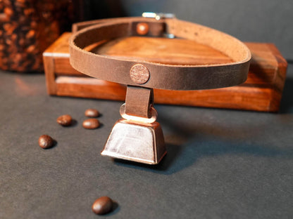 Brown leather hucow choker with a metal cowbell pendant on a dark surface
