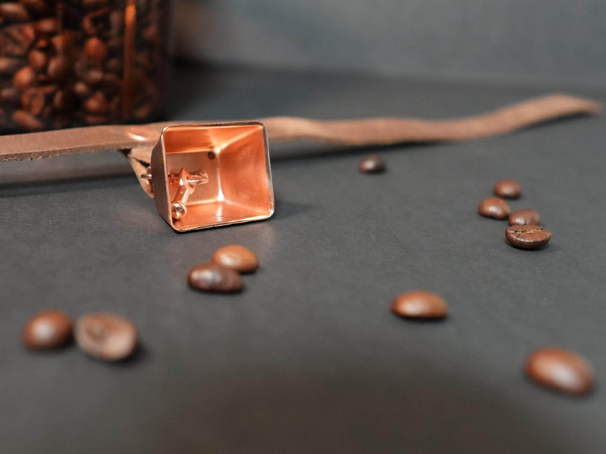 Close-up of a rose gold hucow choker with coffee beans scattered on a dark surface