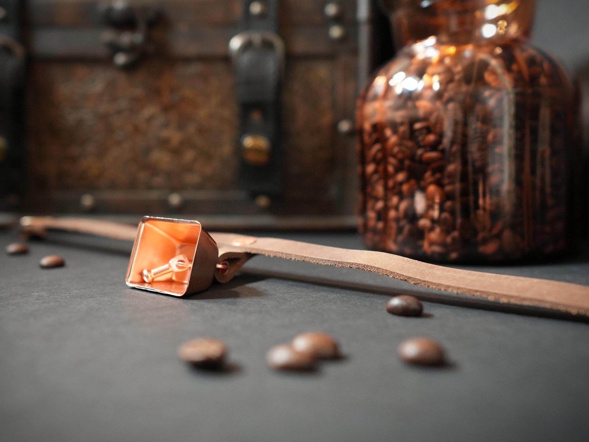 Bound by Dave hucow choker with copper bell and leather strap on dark surface with coffee beans