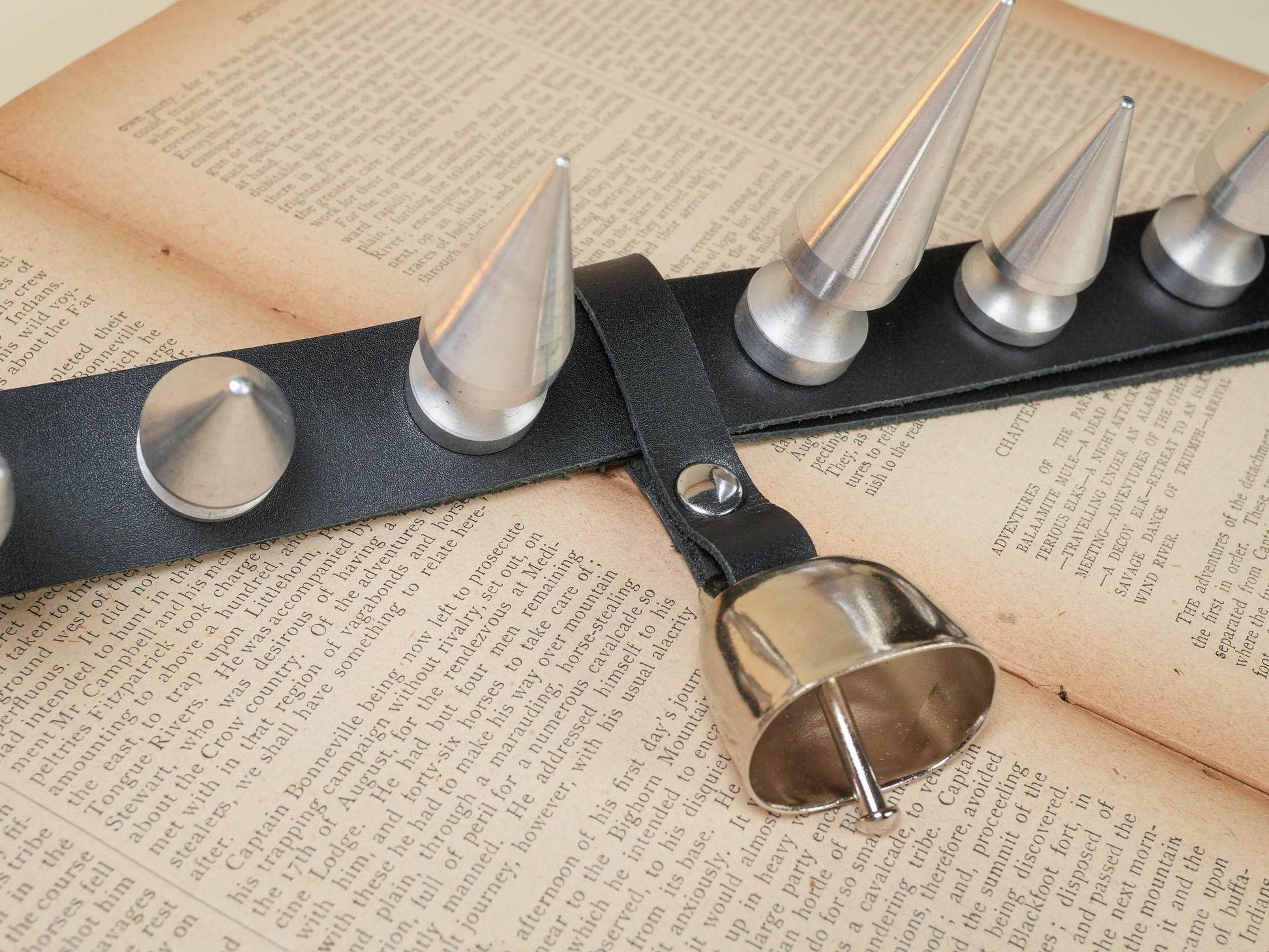 Bound by Dave black leather hucow collar with metal spikes and attached bell on open book pages