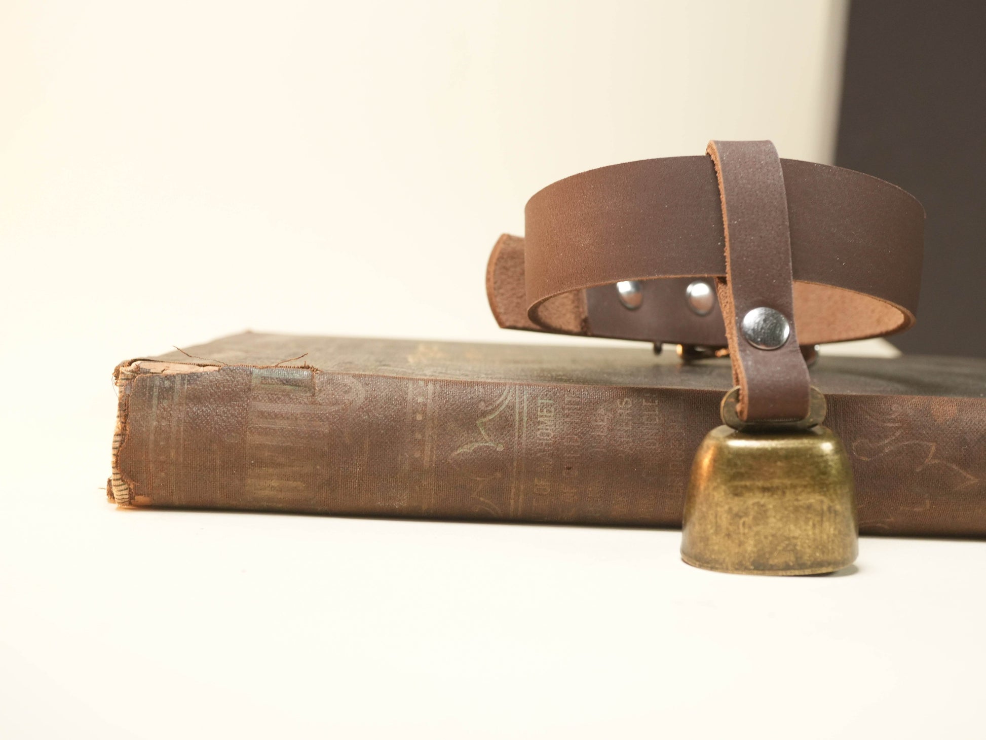 Bound by Dave brown leather Hucow Collar with brass bell placed on vintage book
