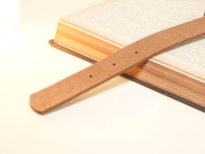 Close-up of Bound by Dave Hucow Collar brown leather strap with adjustment holes on book background