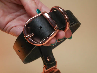 Black leather Hucow Collar with rose gold buckle and ring held in hand from Bound by Dave
