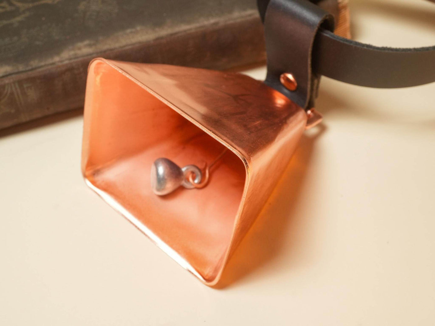 Copper Hucow Collar bell attached to a black leather strap by Bound by Dave