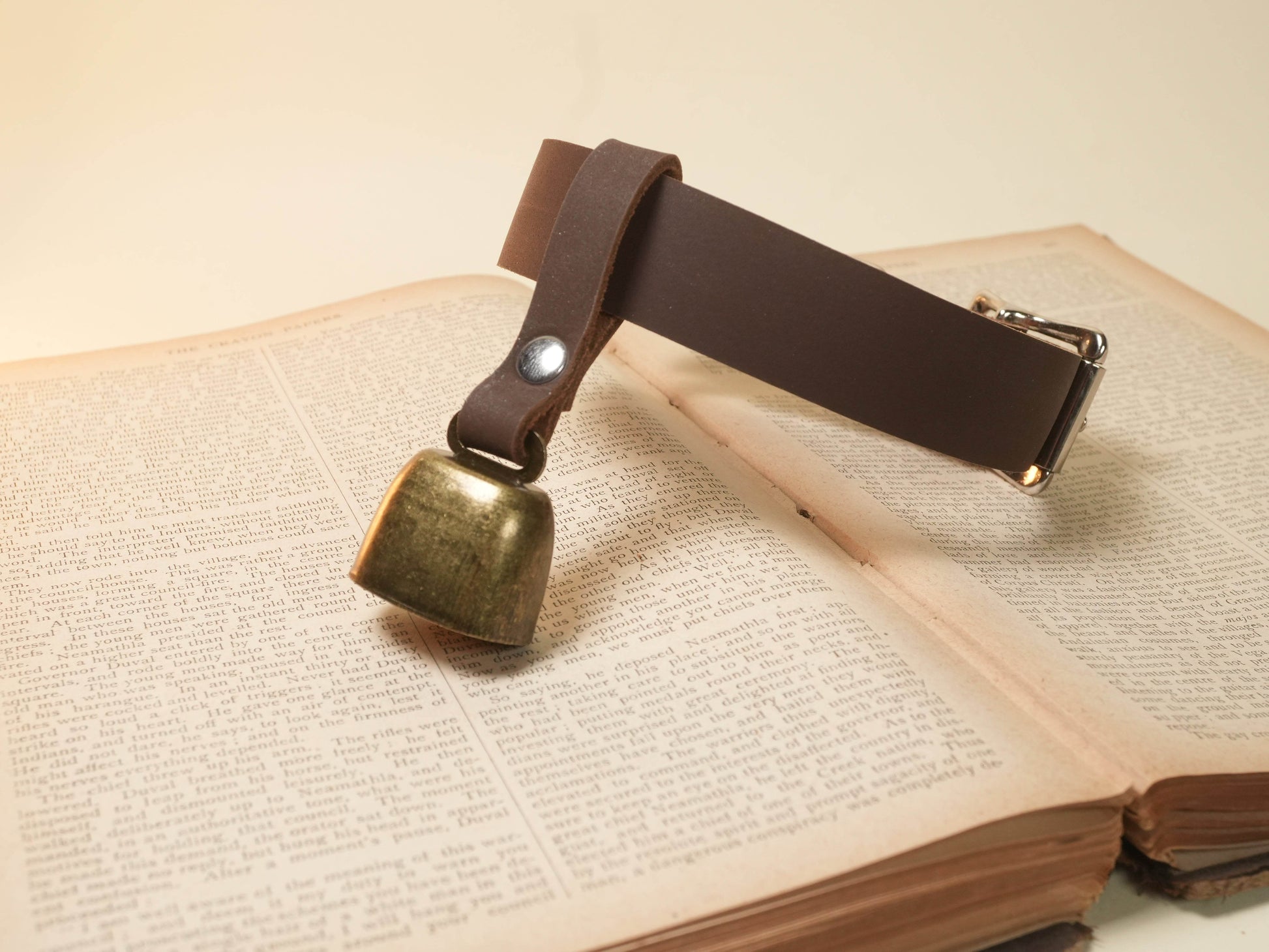 Bound by Dave Hucow Collar with brown leather strap and brass bell on vintage book background