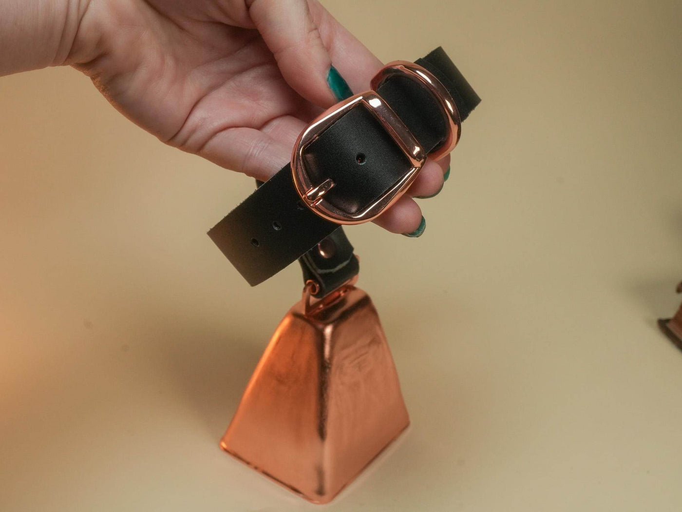 Black leather Hucow Collar with rose gold buckle and large copper cowbell held in hand