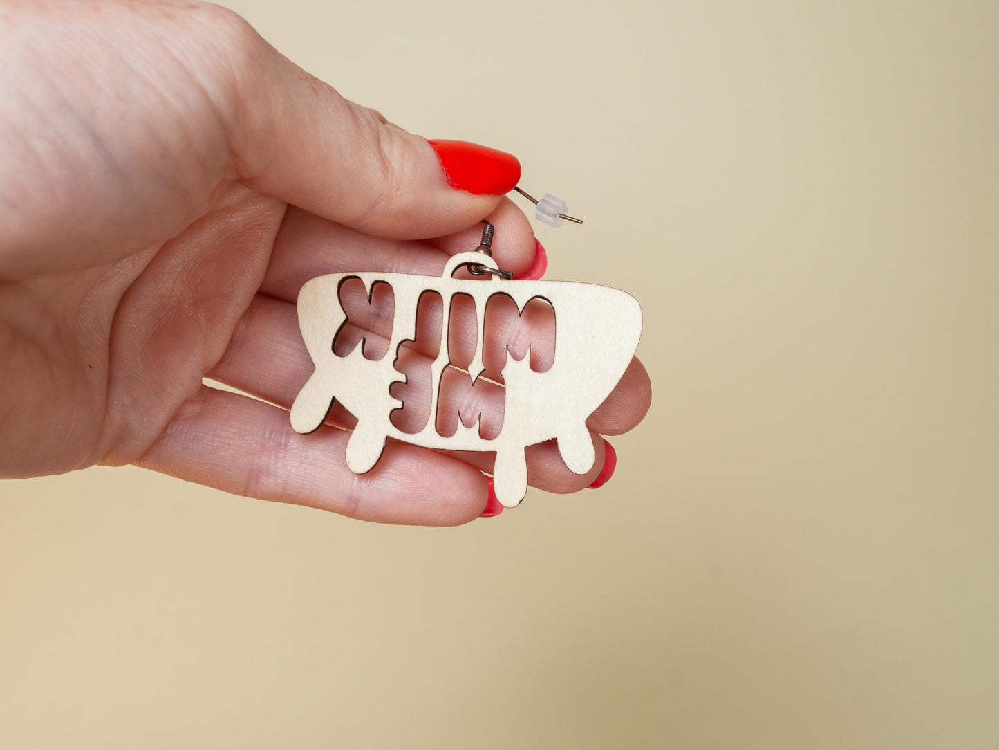 Hand holding Bound by Dave Hucow Earrings shaped like a dripping milk sign with red nail polish