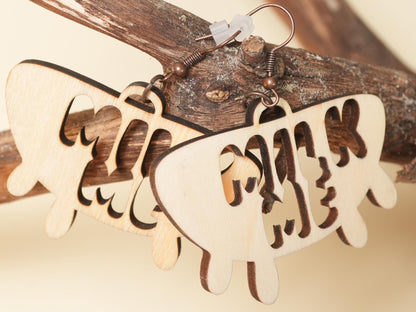 Wooden drip-shaped Hucow Earrings with cutout text hanging on rustic branch by Bound by Dave