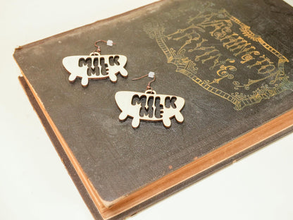 Hucow Earrings shaped like a milk splash with the word milk on vintage book background