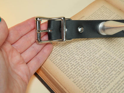 Black leather hucow collar with metal buckle held in a hand over an open book