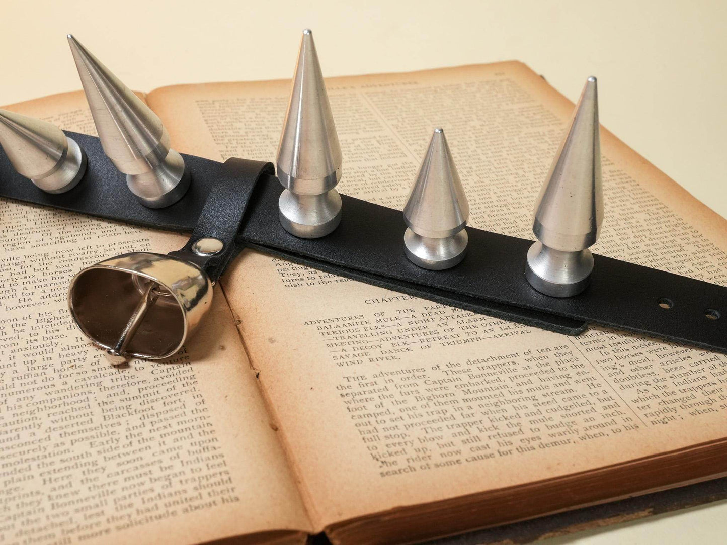 Bound by Dave hucow leather strap with large metal spikes and attached metal bell on open book