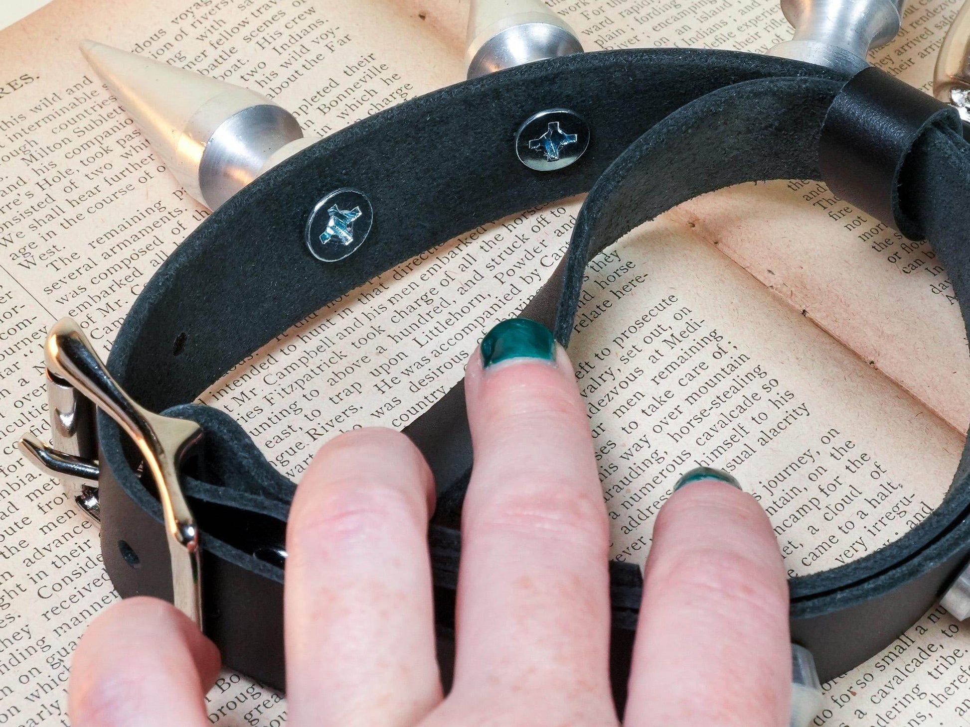 Hand holding a black leather spiked collar from Bound by Dave featuring metal spikes and buckle closure for hucow play