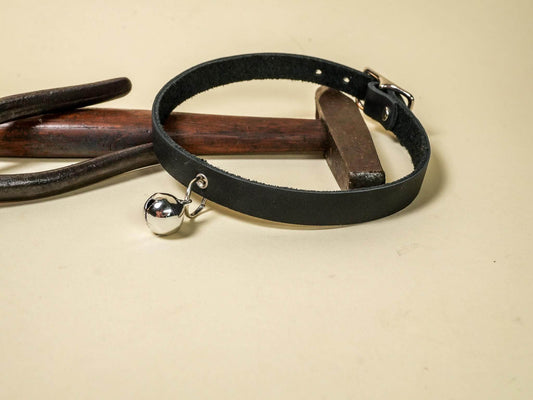 Black leather kitten collar with silver bell and buckle by Bound by Dave on wooden surface