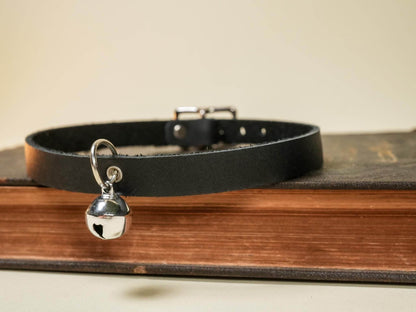 Bound by Dave black kitten collar with silver bell resting on a closed vintage book
