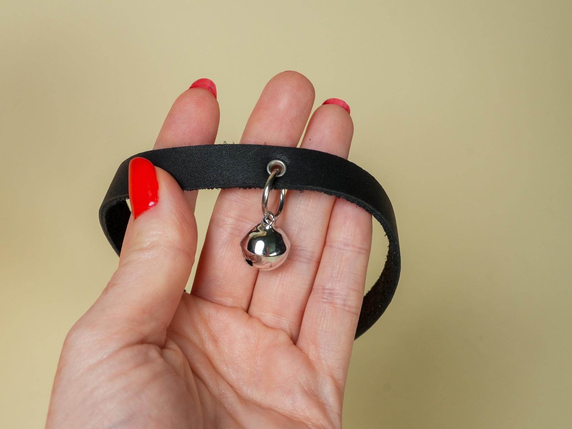Black kitten collar with a silver bell held in hand with red nail polish by Bound by Dave